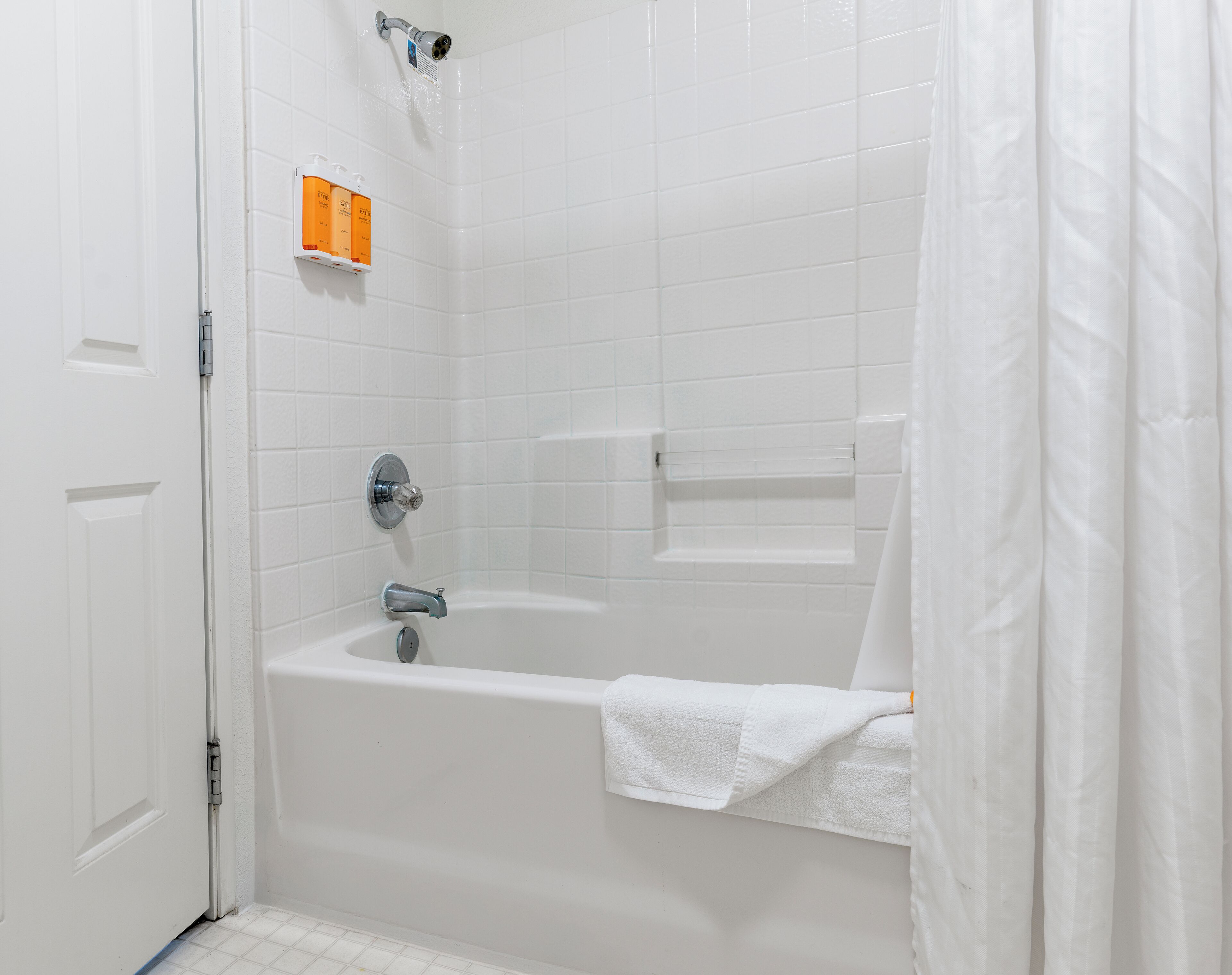 A white tiled bathroom with a bathtub, a showerhead, and a towel rack.