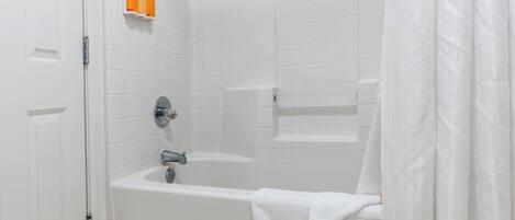 A white tiled bathroom with a bathtub, a showerhead, and a towel rack.