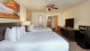 Una habitación de hotel con dos camas, un escritorio con televisor y microondas, ventilador de techo y obras de arte en las paredes.