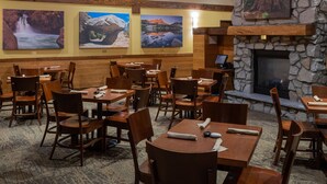 Un restaurante con vigas de madera, paredes de piedra y una chimenea. Mesas y sillas dispuestas para comer.