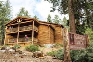 Een houten lodge met balkon, omgeven door bomen en een bordje met de tekst John Muir Lodge bij Kings Canyon National Park.