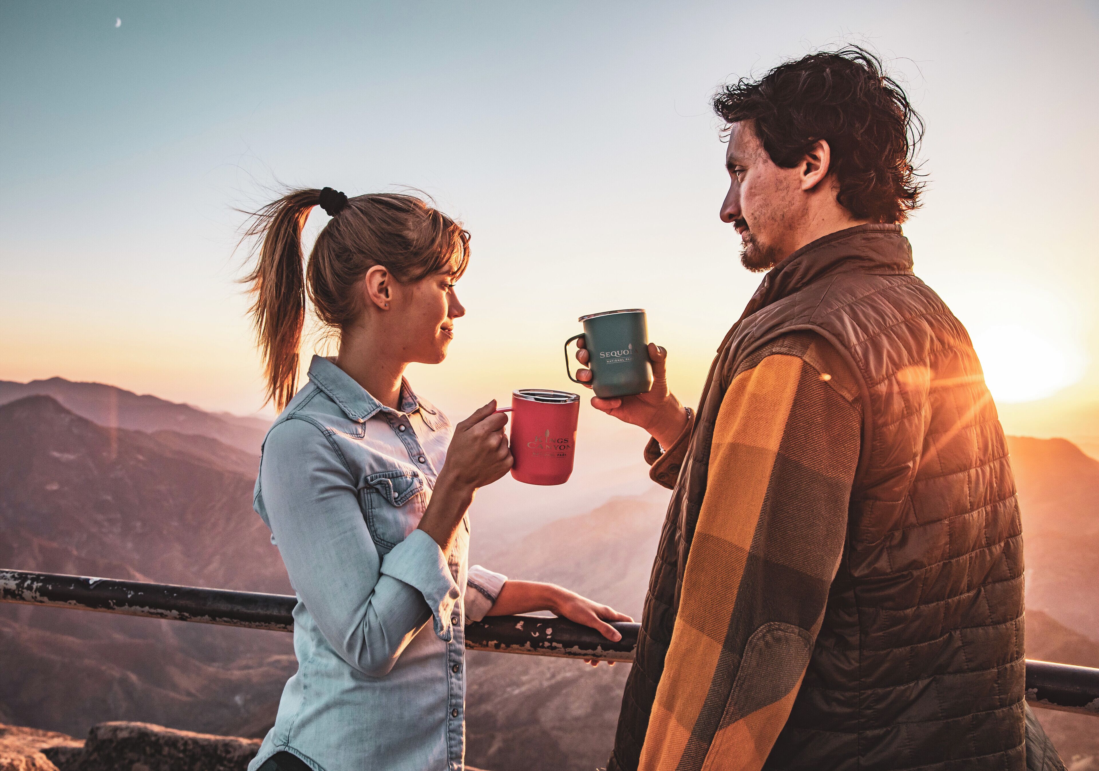 Dos personas sosteniendo tazas, con vistas a un paisaje montañoso.