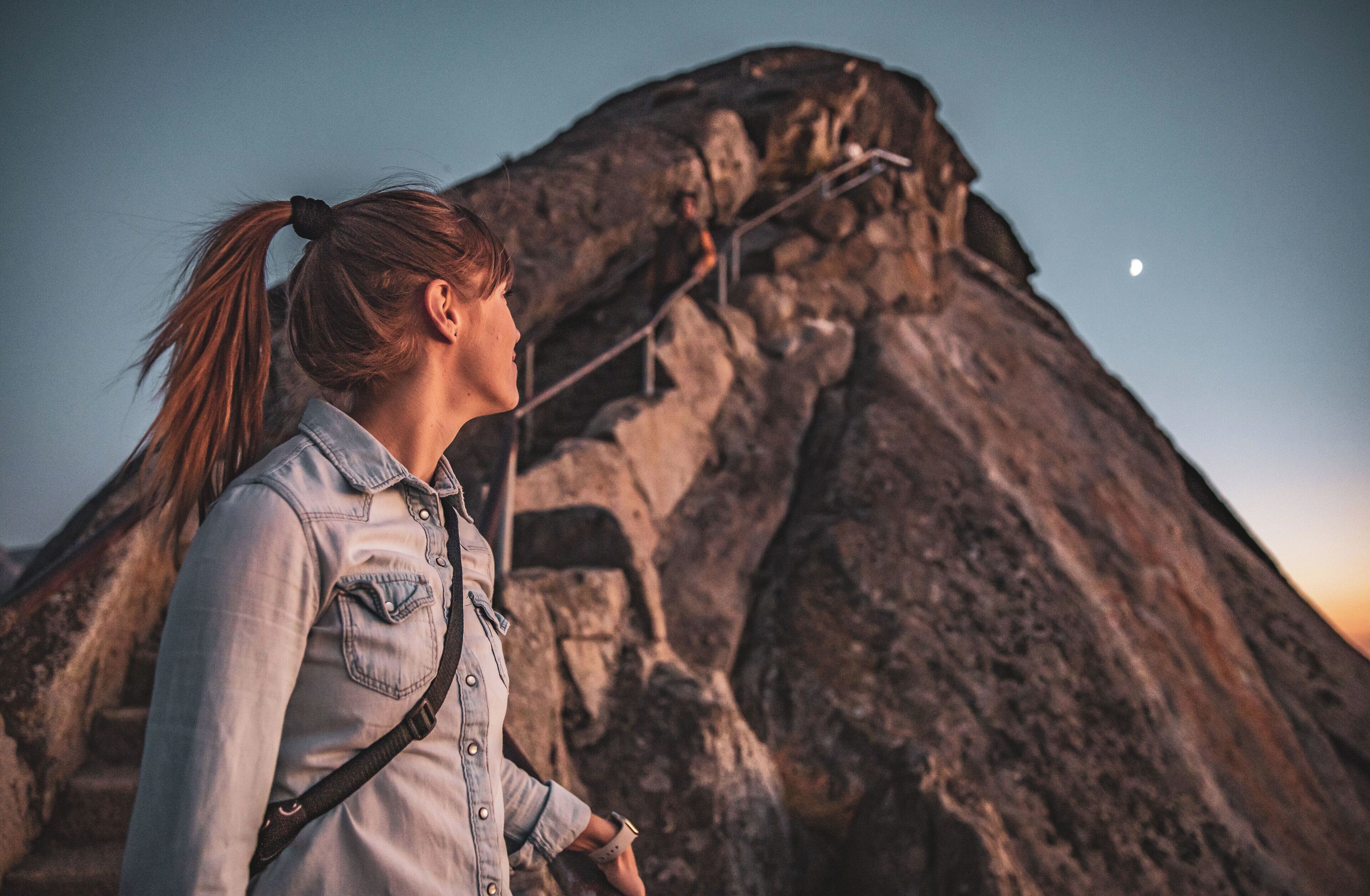 A person standing in front of a rocky mountain with a clear sky.