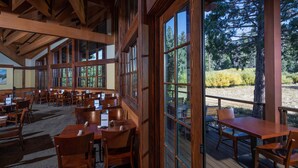 Un amplio comedor interior con mesas y sillas de madera, y grandes ventanales que ofrecen vistas al exterior.