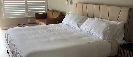 Una cama bien tendida en una habitación con techo inclinado, un aplique de pared y una ventana con persianas.