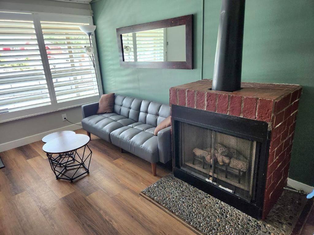 A living room with a gray sofa, a round coffee table, a fireplace, and a window with blinds.
