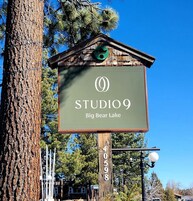 Big Bear Lake -järvellä sijaitsevan Studio 9 -studion opastekyltti, jossa on näkyvillä maalaishenkinen puinen rakennelma, vihreä katto ja valkoinen kyltti.