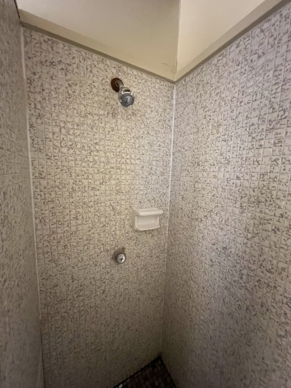 A small, tiled shower stall with a white soap dish and a faucet.