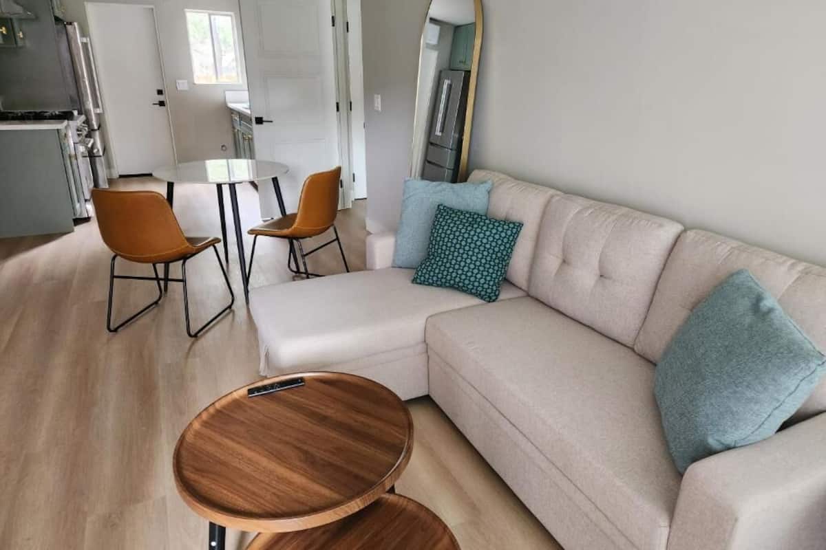 A modern living room with a sofa, two chairs, a coffee table, and a kitchen in the background.