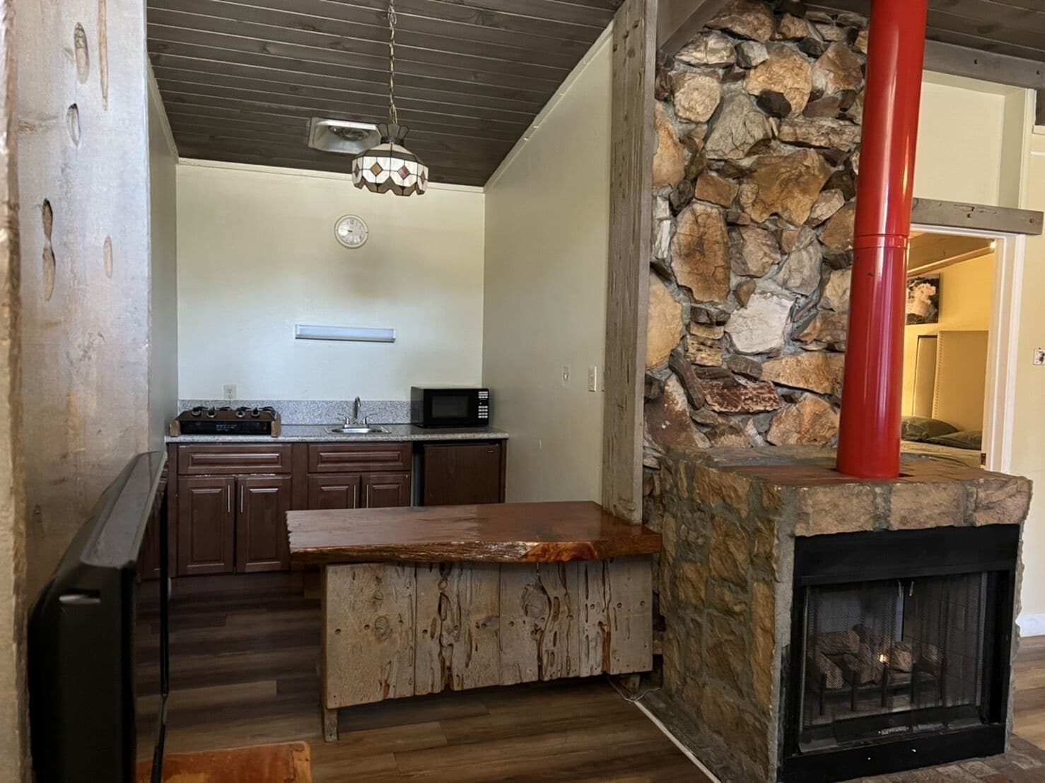 A modern kitchen with a stone fireplace, wooden bar, and a hanging light fixture.