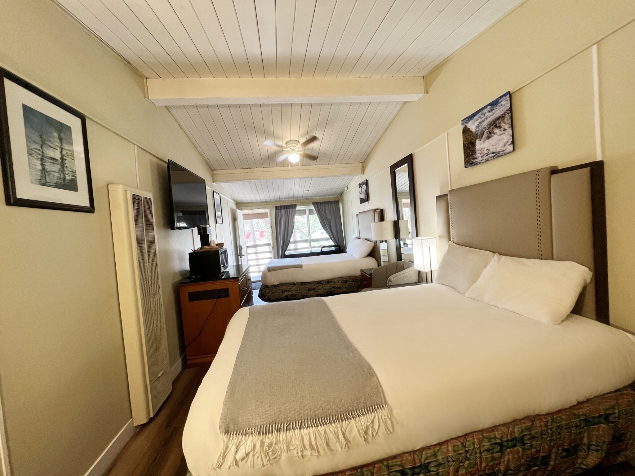 A hotel room with a large bed, a smaller bed, a desk with a television, and a ceiling fan.