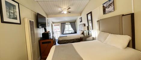A hotel room with a large bed, a smaller bed, a desk with a television, and a ceiling fan.
