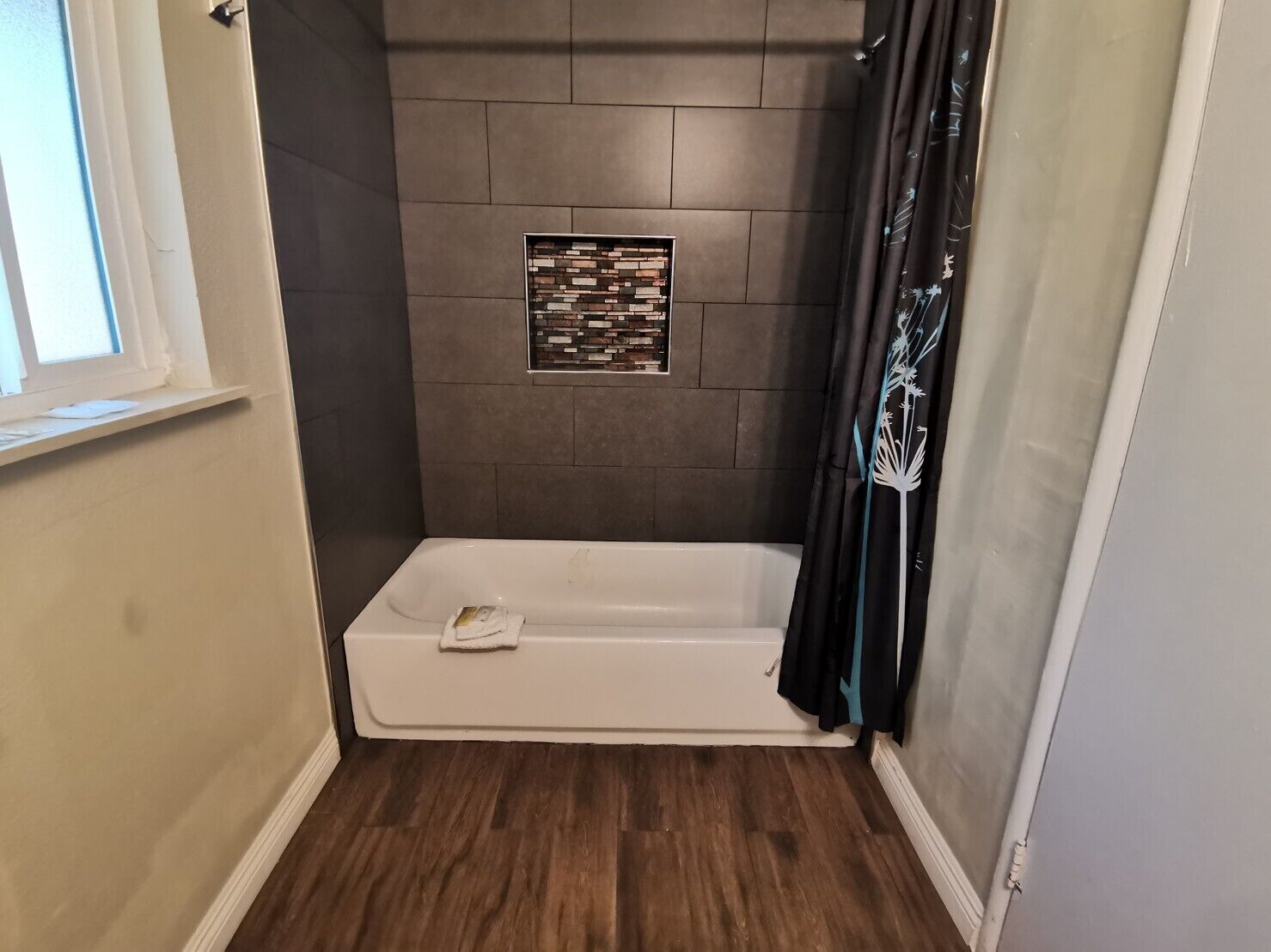 A small, modern bathroom with a shower, a window, and a decorative tile wall.
