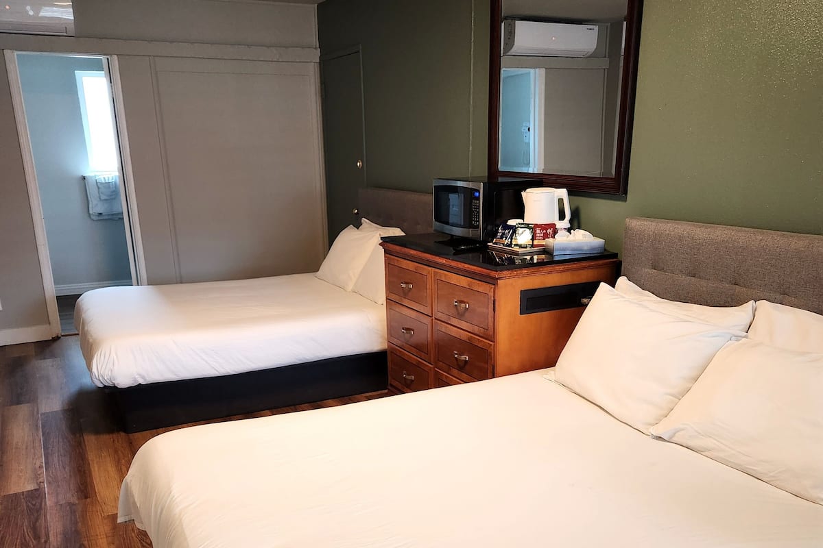 A hotel room with two beds, a wooden dresser, a microwave, and a mirror on the wall.