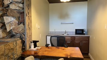 Uma cozinha compacta com parede de pedra decorativa, uma mesa de jantar de madeira, uma cadeira de escritório preta e um micro-ondas.