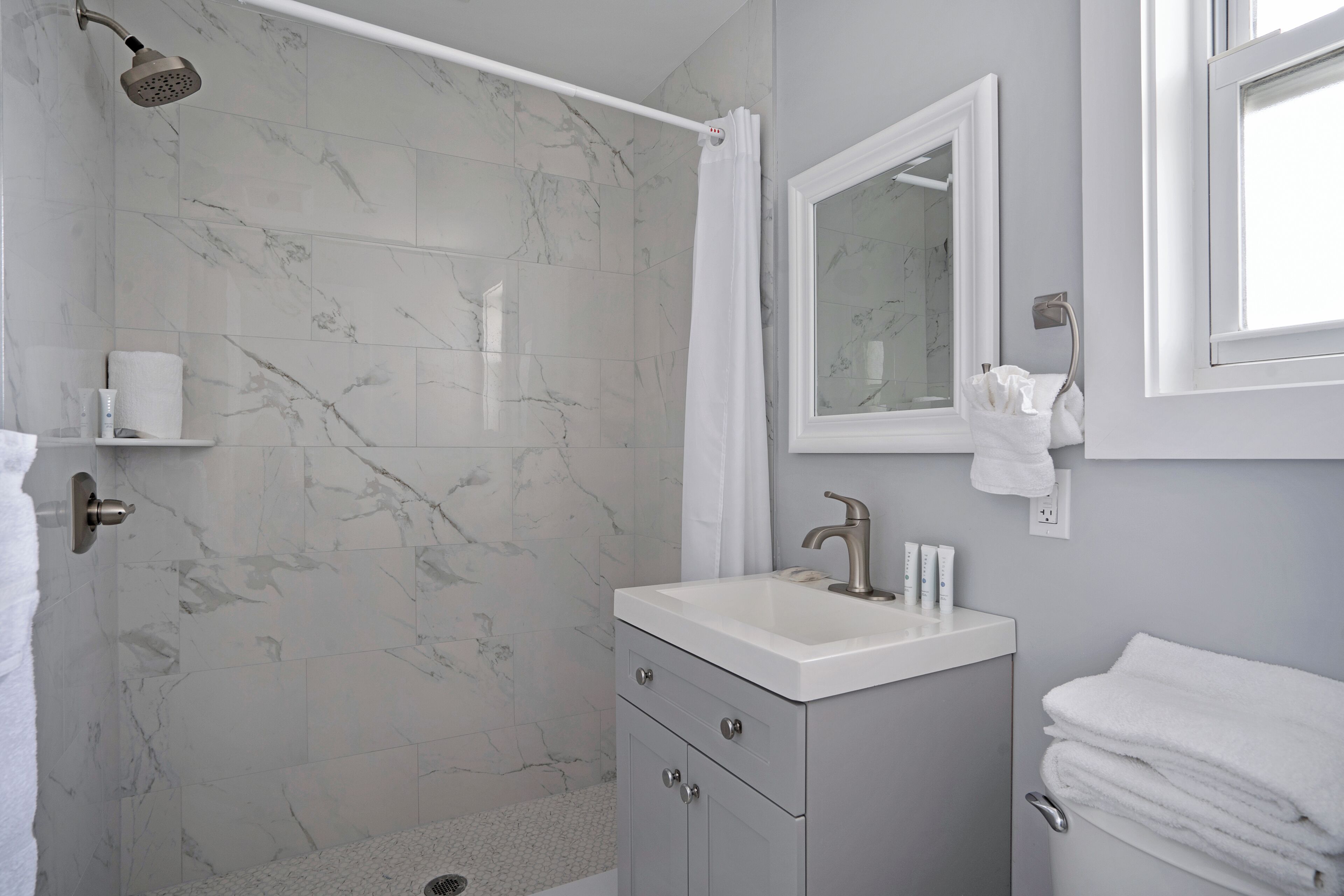 A bathroom with a shower, a sink, a mirror, and a towel rack.