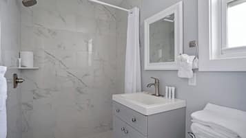 A bathroom with a shower, a sink, a mirror, and a towel rack.