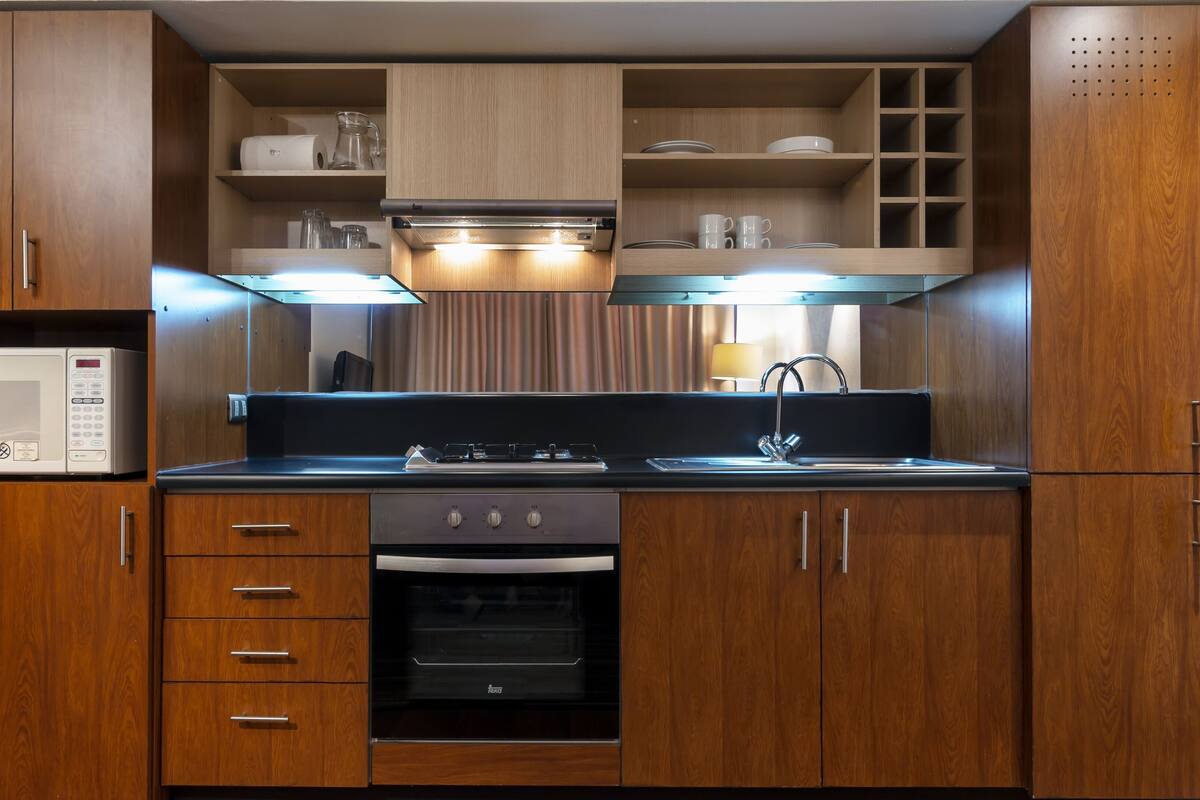 Cocina compacta con armarios de madera, microondas, estufa y horno empotrado.