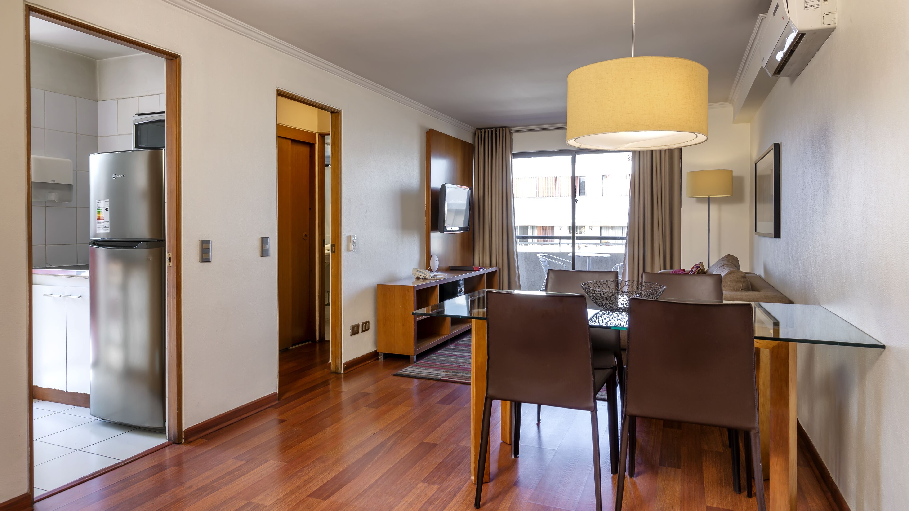 Una camera d'albergo moderna con zona pranzo, angolo cottura e una grande finestra con tende.