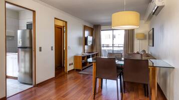 Una camera d'albergo moderna con zona pranzo, angolo cottura e una grande finestra con tende.