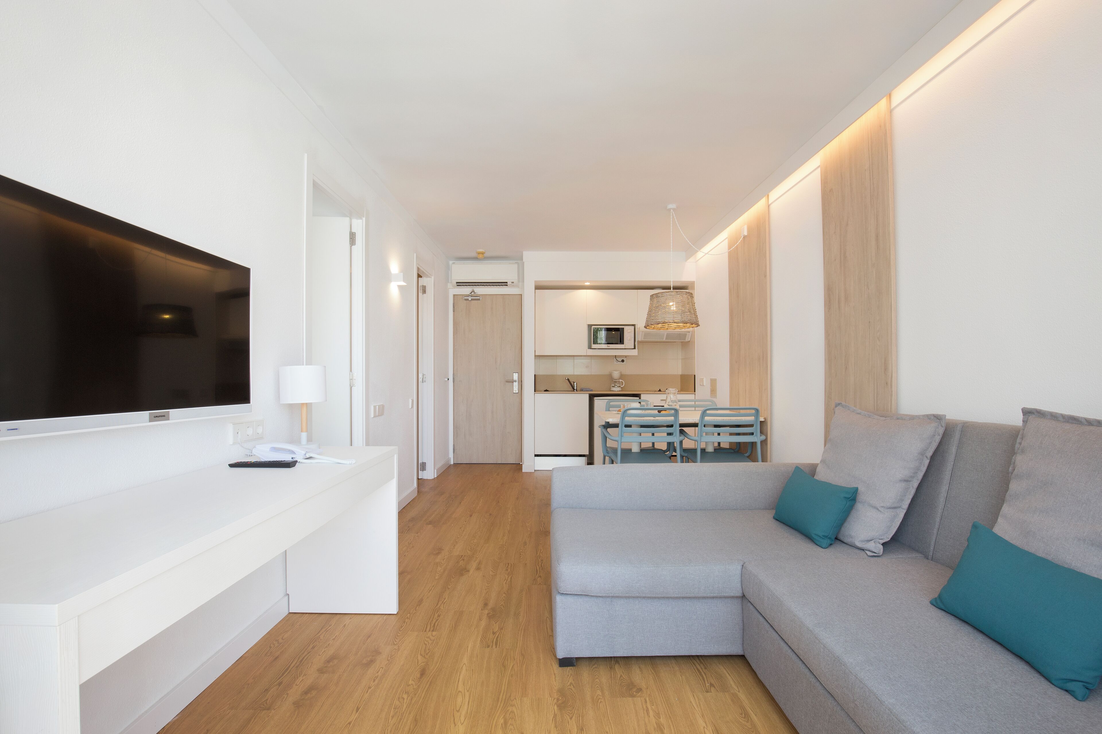 Un salon moderne avec un canapé gris, des coussins turquoise, un téléviseur à écran plat et un plancher en bois.