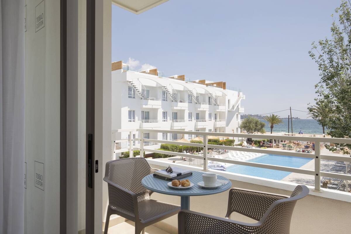 A balcony with a table and chairs, overlooking a pool and a building with multiple balconies.