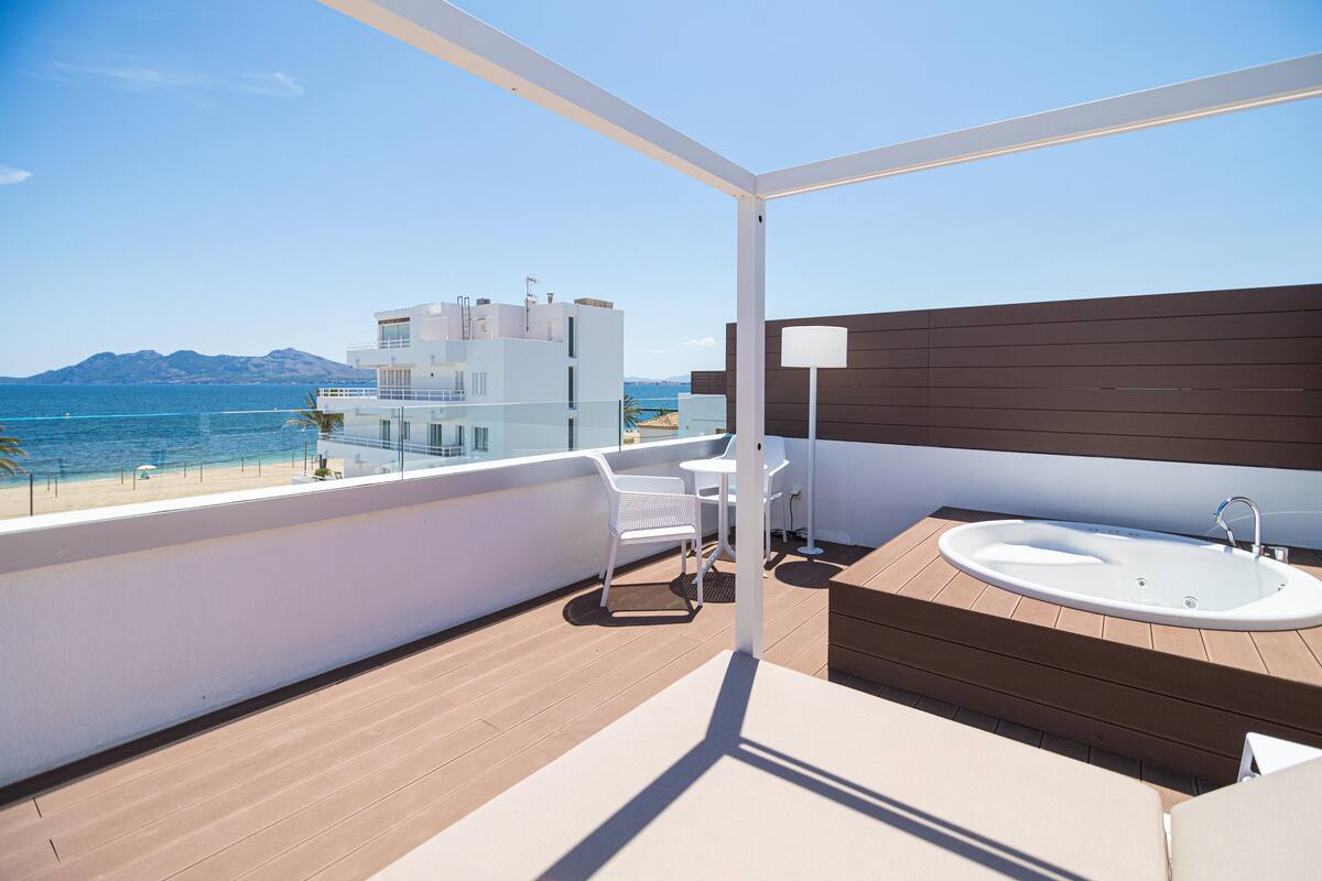 A balcony with a view of the sea, a white chair, a small table, and a bathtub.