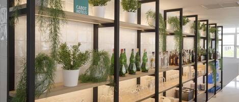 A hotel bar with shelves of glasses, bottles, and potted plants.