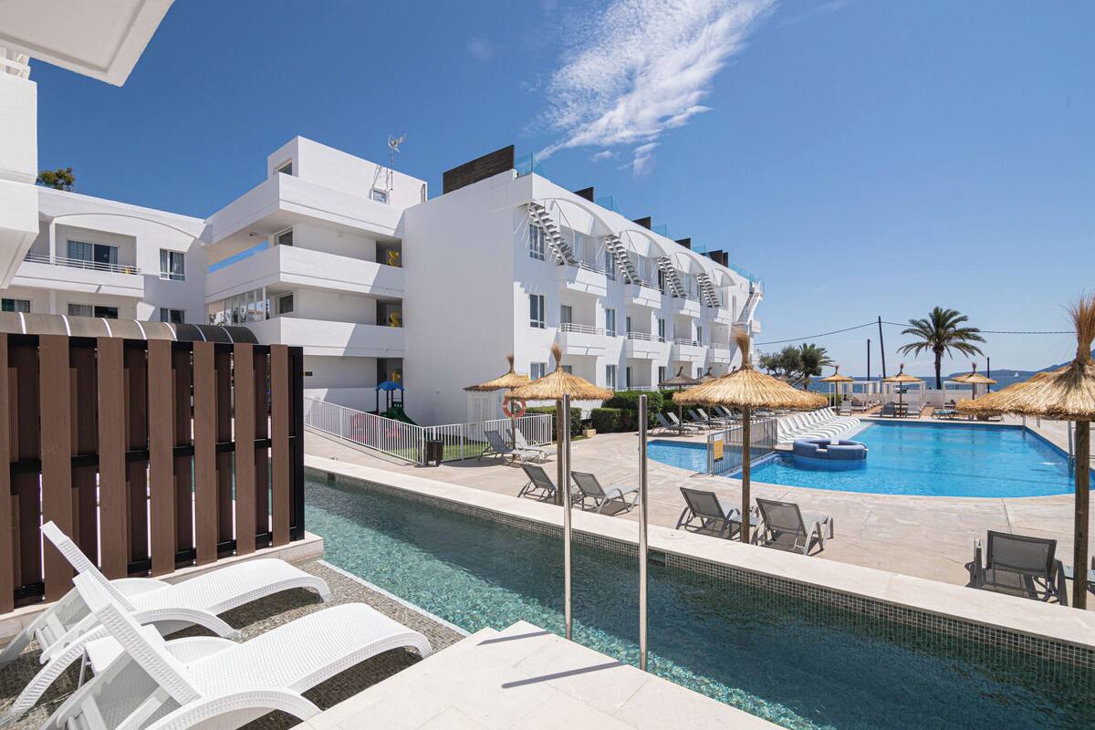 A modern hotel with a swimming pool, sun loungers, and thatched umbrellas.