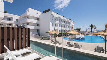 A modern hotel with a swimming pool, sun loungers, and thatched umbrellas.