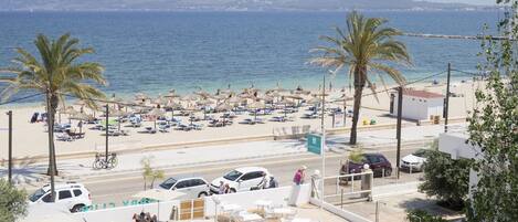 A pool area with lounge chairs and umbrellas, a beach with umbrellas and sun loungers, and a view of the sea and mountains.