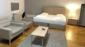 A modern hotel room with a bed, a sofa, a small table, and a nightstand. - Mosebacke Hostel (Stockholm)