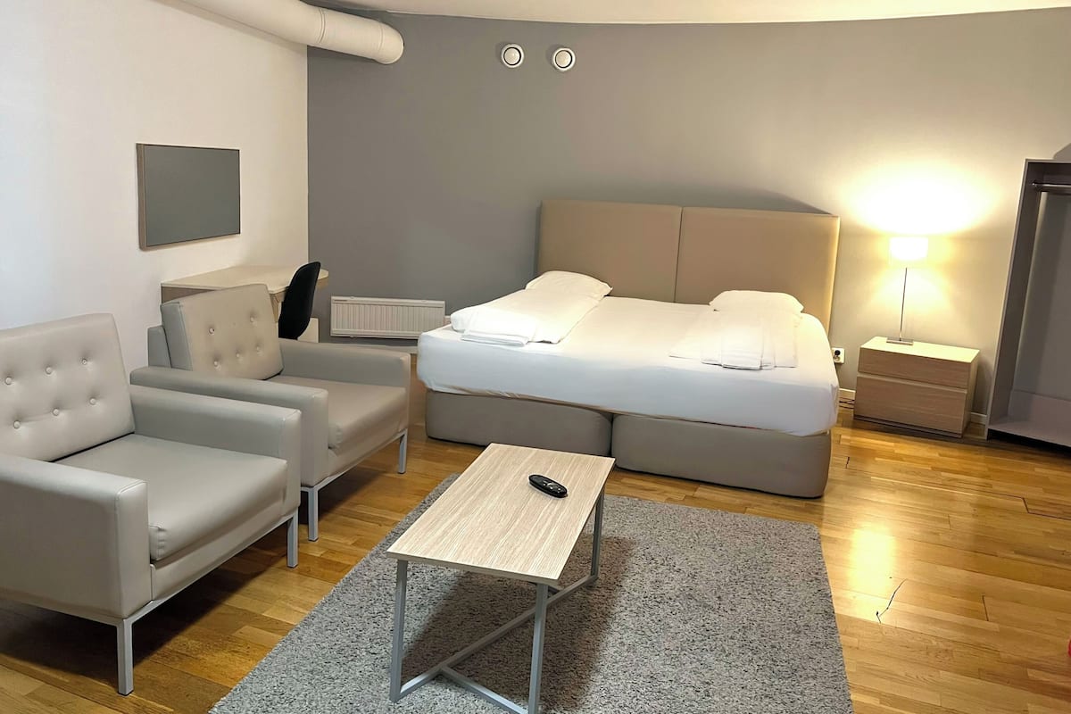 A modern hotel room with a bed, a sofa, a small table, and a nightstand.