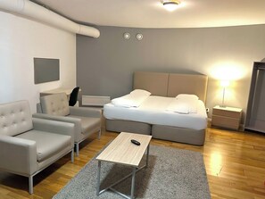 A modern hotel room with a bed, a sofa, a small table, and a nightstand. - Mosebacke Hostel (Stockholm)