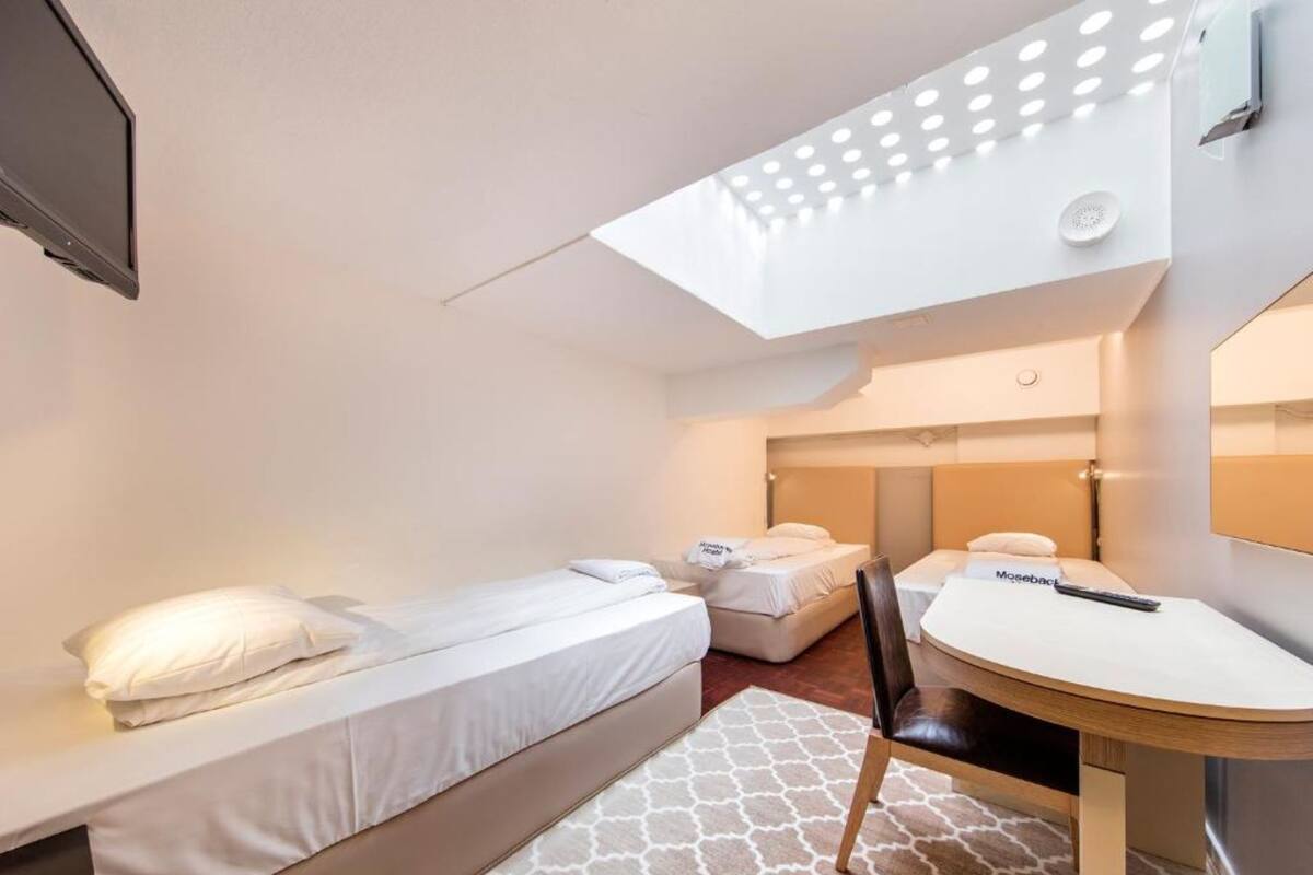 A hotel room with two beds, a desk, a chair, and a skylight.