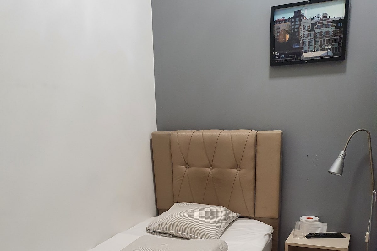 A single bed with a headboard, a bedside table with a lamp, and a framed picture on the wall.
