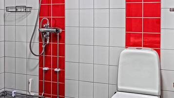 Un baño con inodoro blanco, pared de ducha con azulejos rojos y suelo de baldosas negras.