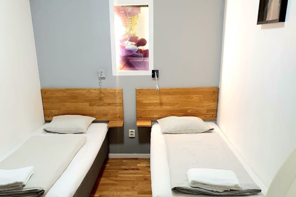 A room with two beds, a small window, and a white chair.