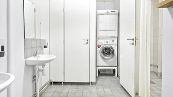 Un baño de hotel pequeño con lavamanos, espejo y una unidad apilada de lavadora y secadora.