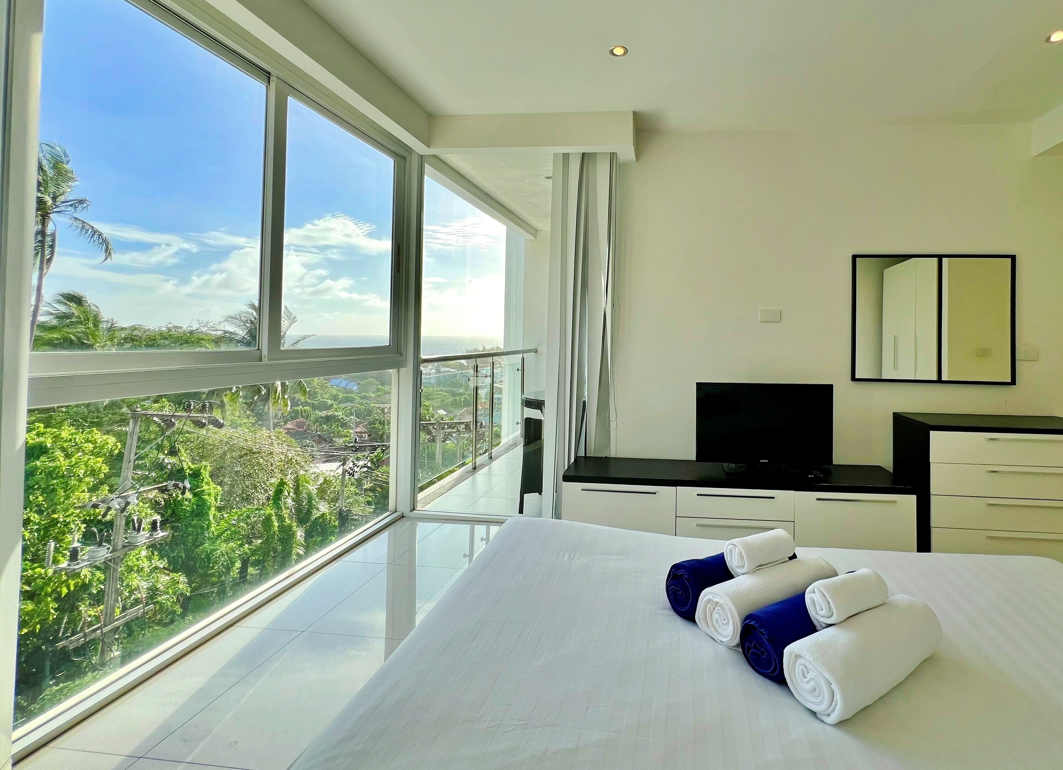 Ein modernes Hotelzimmer mit großzügigem Balkon, einem Bett mit ordentlich gefalteten Handtüchern, einem Flachbildfernseher und minimalistischem Design.