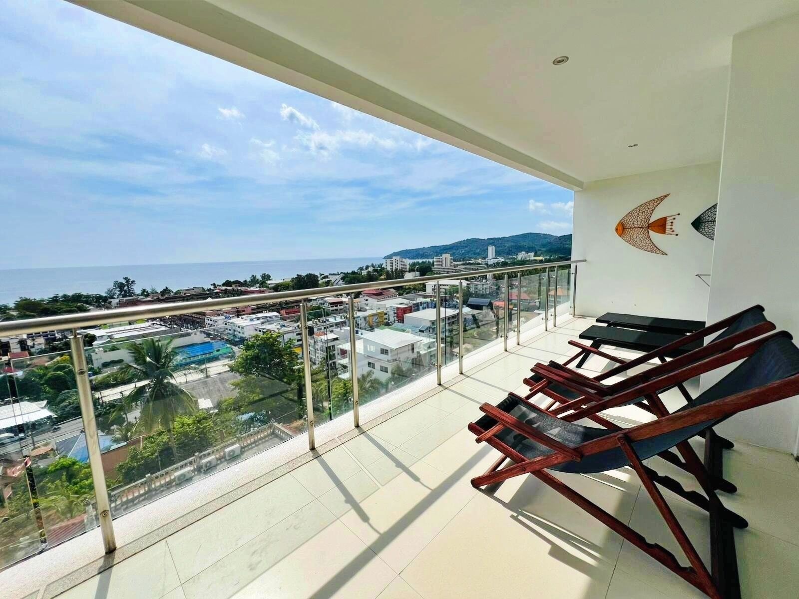 A balcony with a view of the sea and cityscape, equipped with wooden loungers.