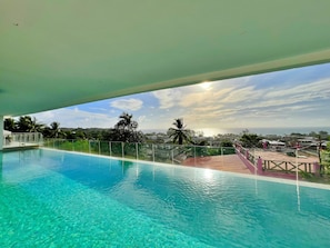 Vista despejada de una piscina con barrera de cristal, rodeada de vegetación y vista al mar.