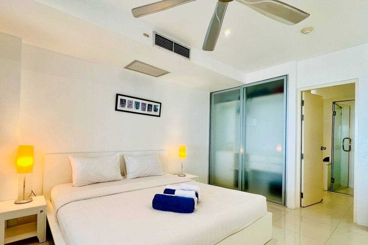 Una habitación de hotel moderna con una cama grande, dos lámparas de noche, una fotografía enmarcada en la pared y un armario con puerta corredera.