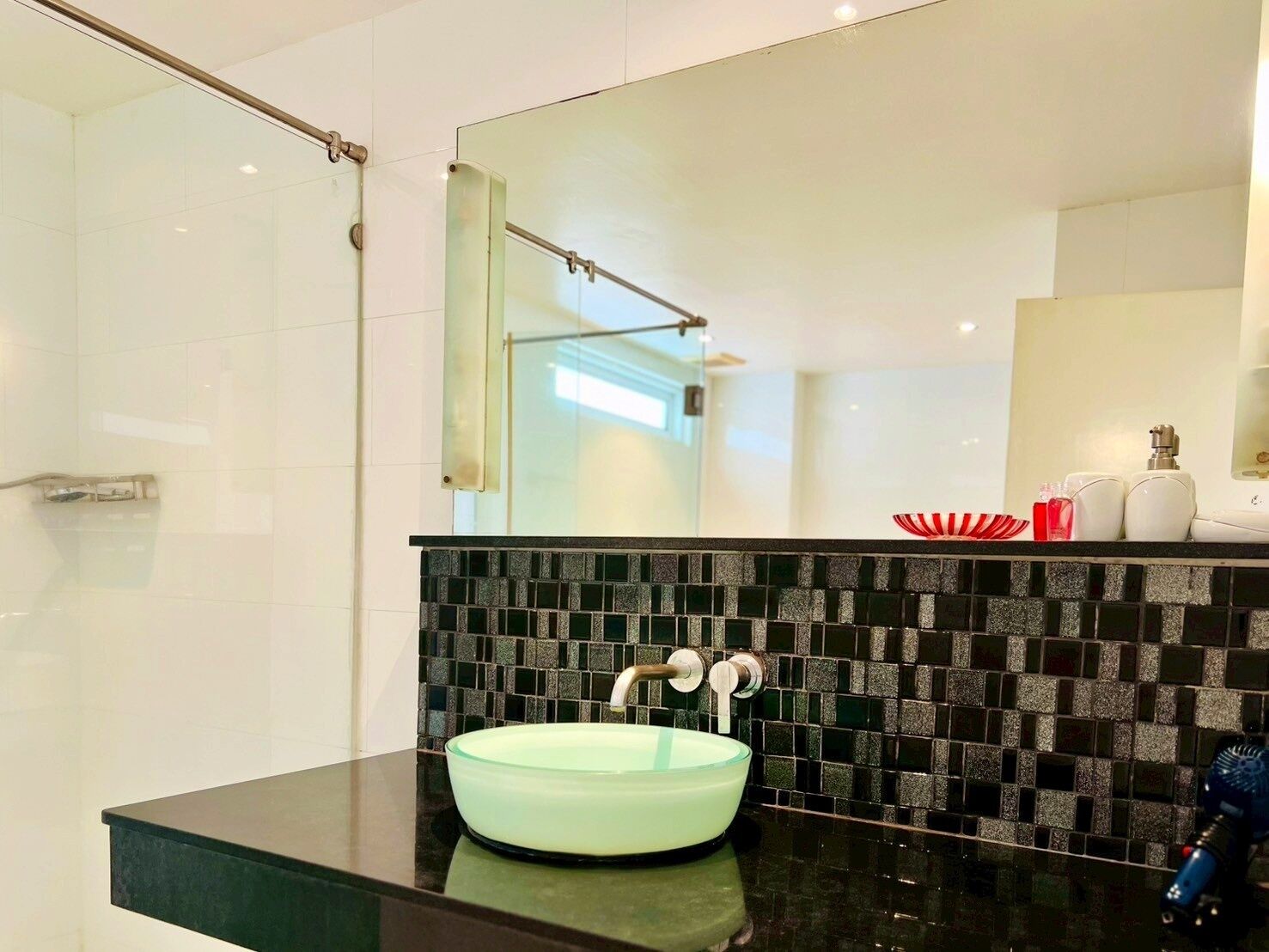 A modern bathroom with a glass sink, black tiled backsplash, and a large mirror.