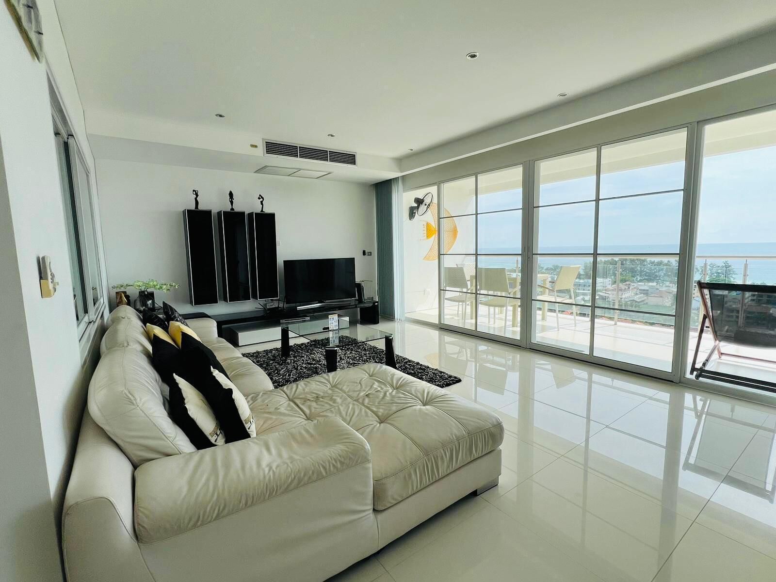 A modern living room with a large window, a sofa, a flat-screen TV, and a sound system.