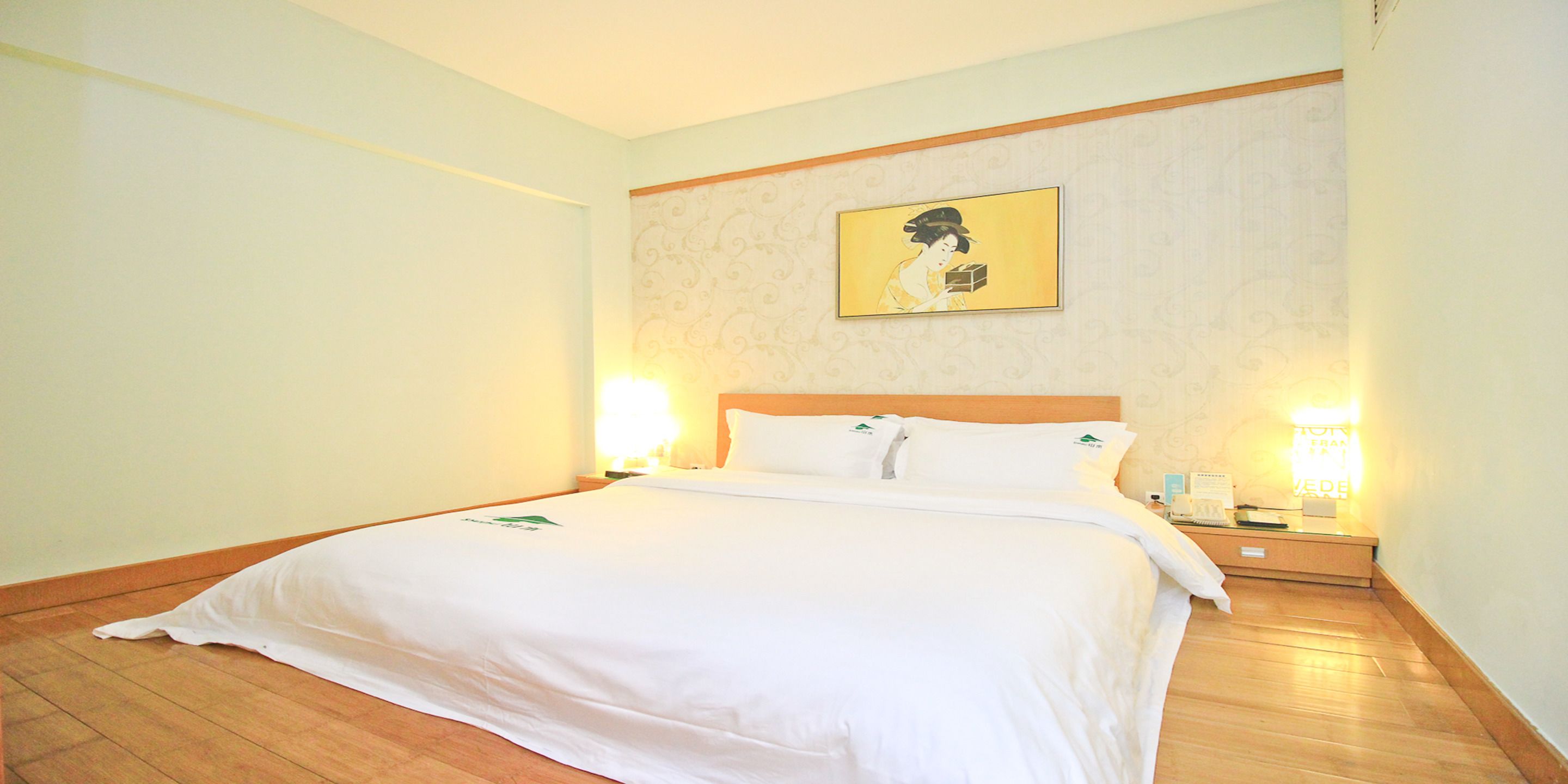 Una habitación de hotel con una cama grande, dos mesitas de noche, una obra de arte colgada en la pared y suelo de madera.