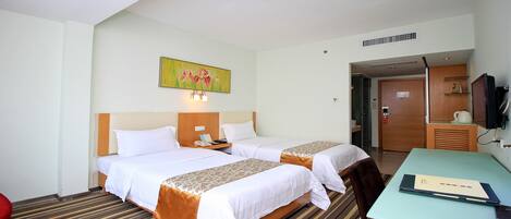 A hotel room with two beds, a desk, a chair, a painting on the wall, and a door leading to a bathroom.