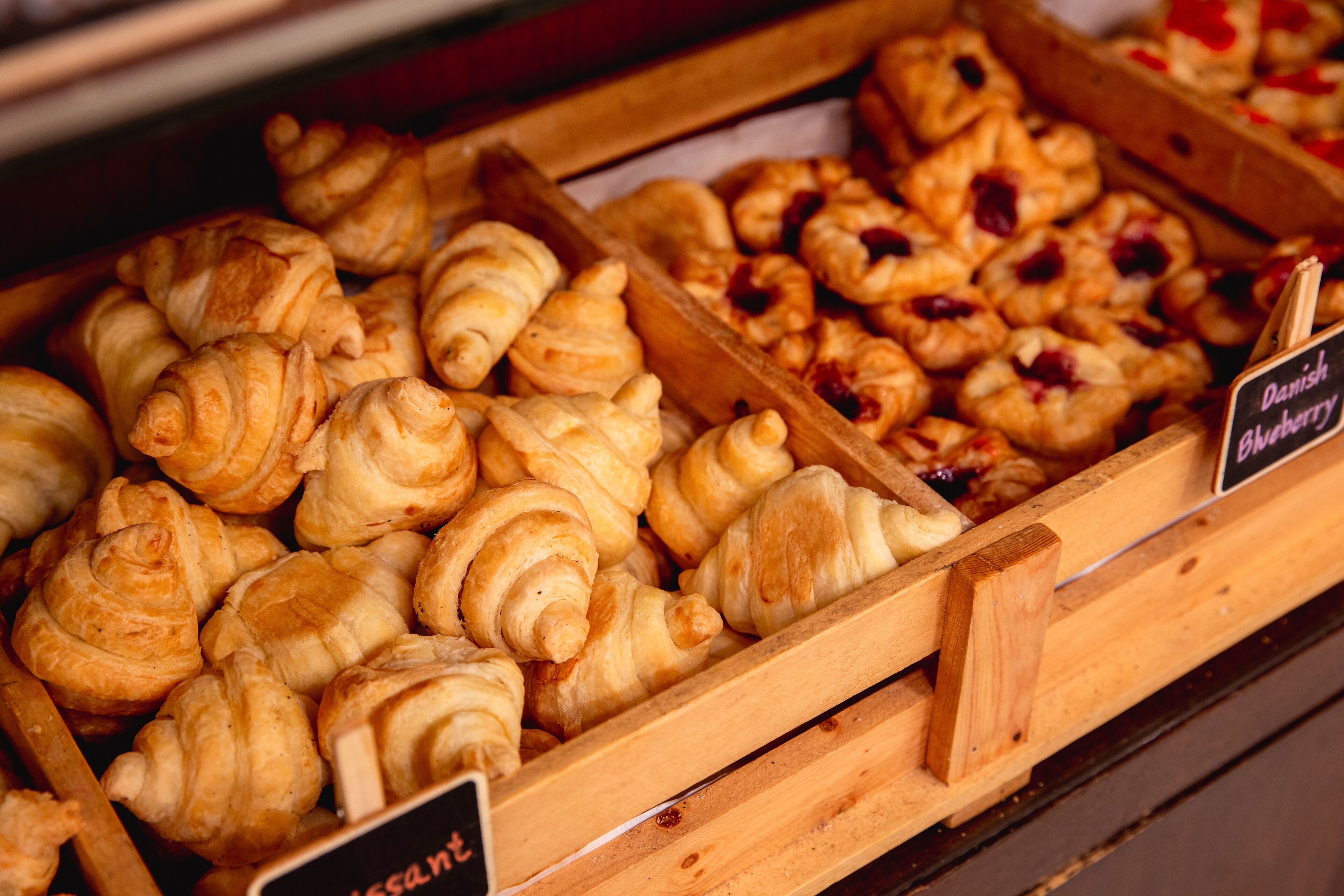 Verschiedene Backwaren in Holzeinlagen, darunter Croissants und Blaubeerkuchen.