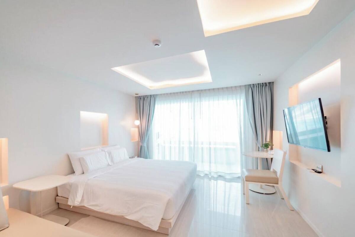 A modern hotel room with a large bed, bedside tables, a desk, and a TV.