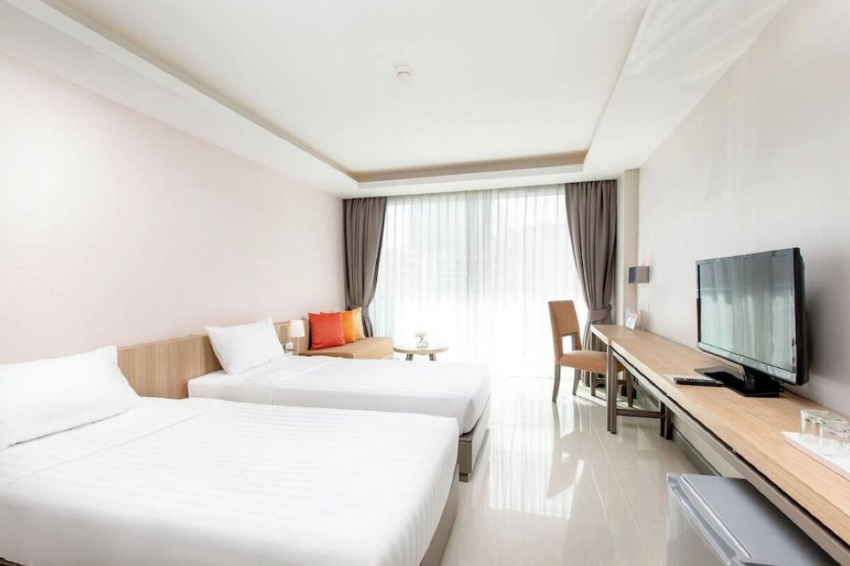 A hotel room with two beds, a desk with a television, and a window with curtains.